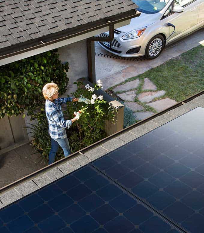 A woman is pruning her rose bushes at her home powered by Sea Bright Solar. 