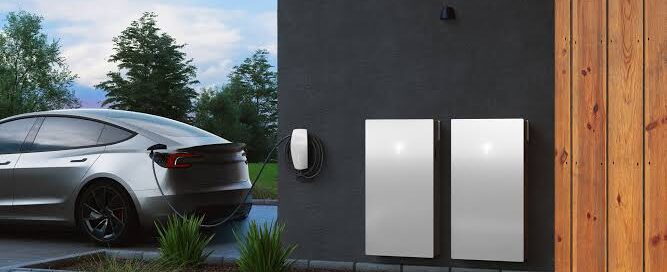 Electric vehicle parked beside a home wall with two battery storage units and an EV charger.