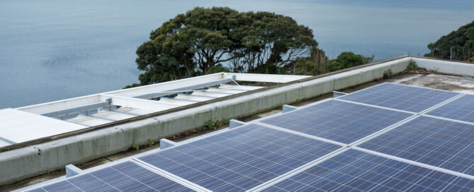 Coastal rooftop solar panels overlooking the ocean under cloudy skies.